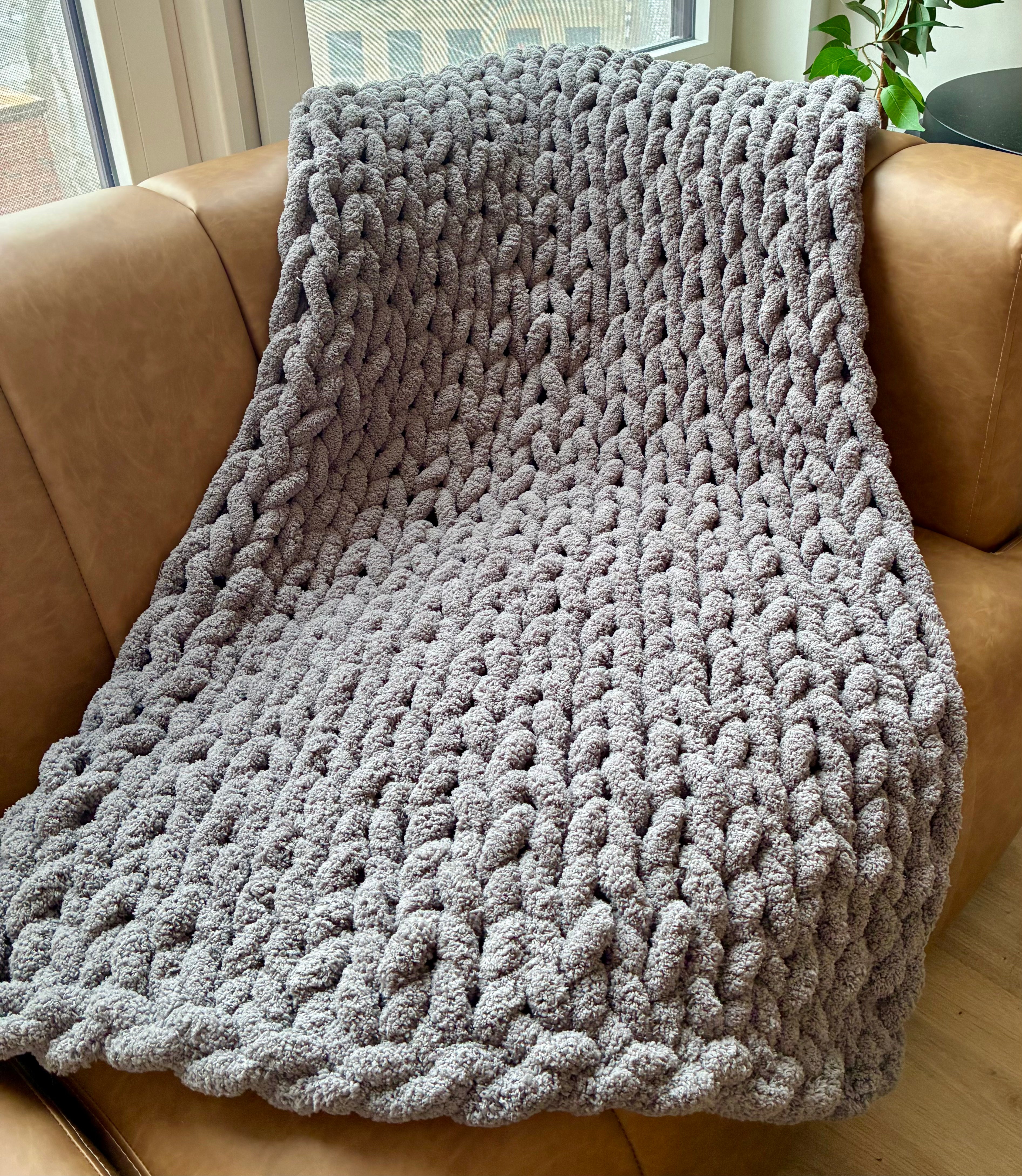 Gray knitted blanket draped over a brown leather couch.