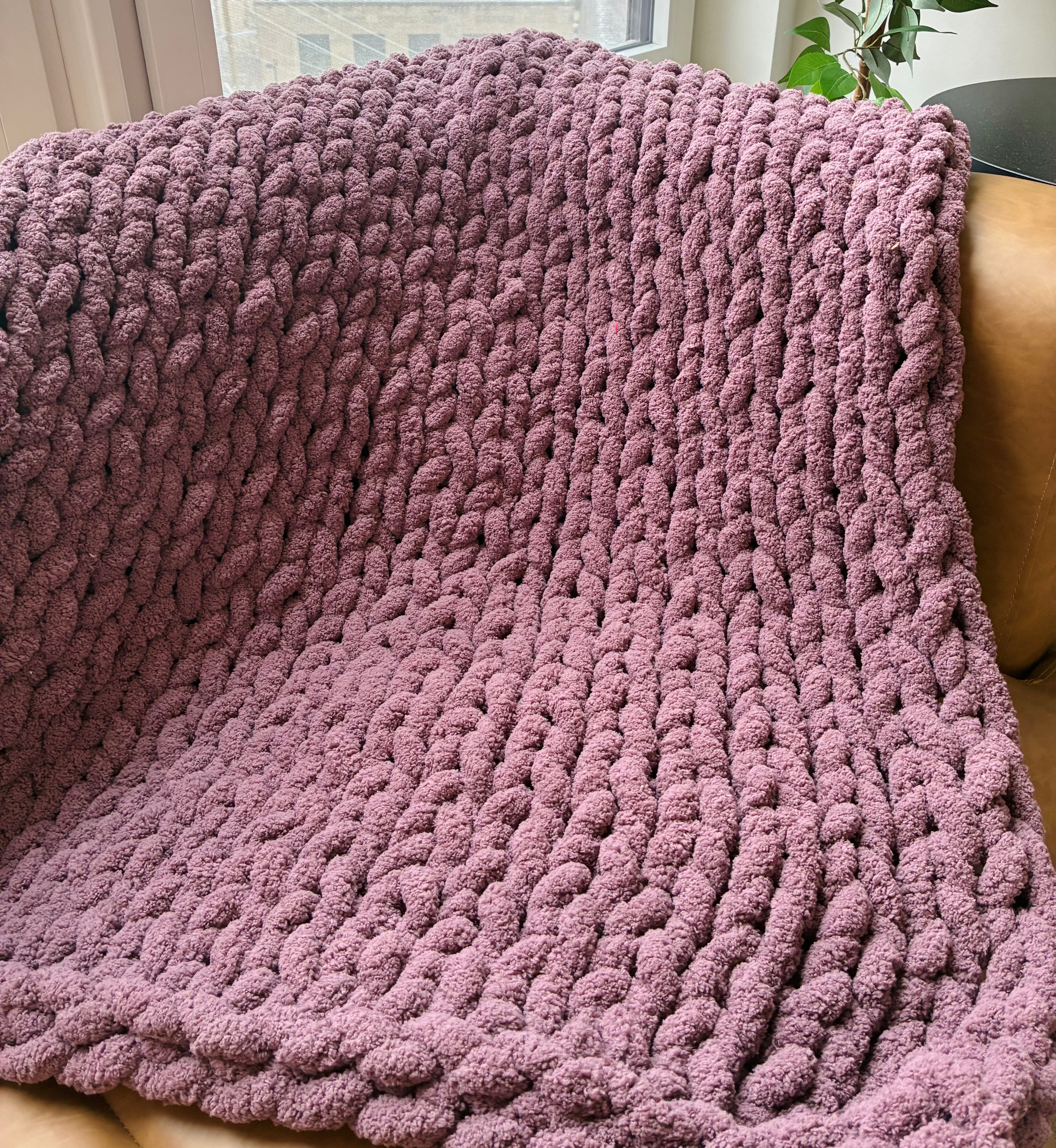 Pink knitted blanket draped over a chair with a blurred background