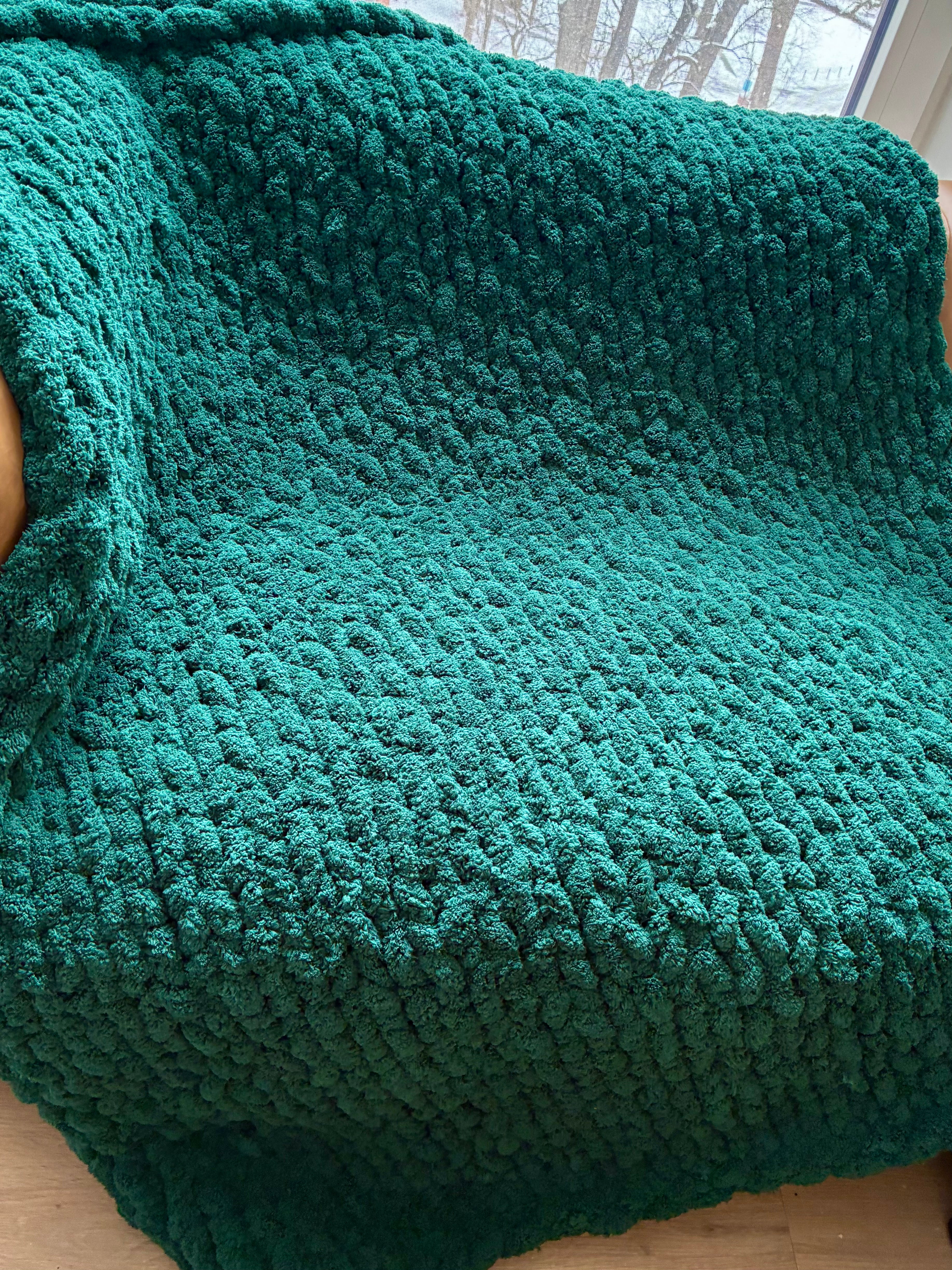 Green knitted blanket on a wooden surface with a window in the background